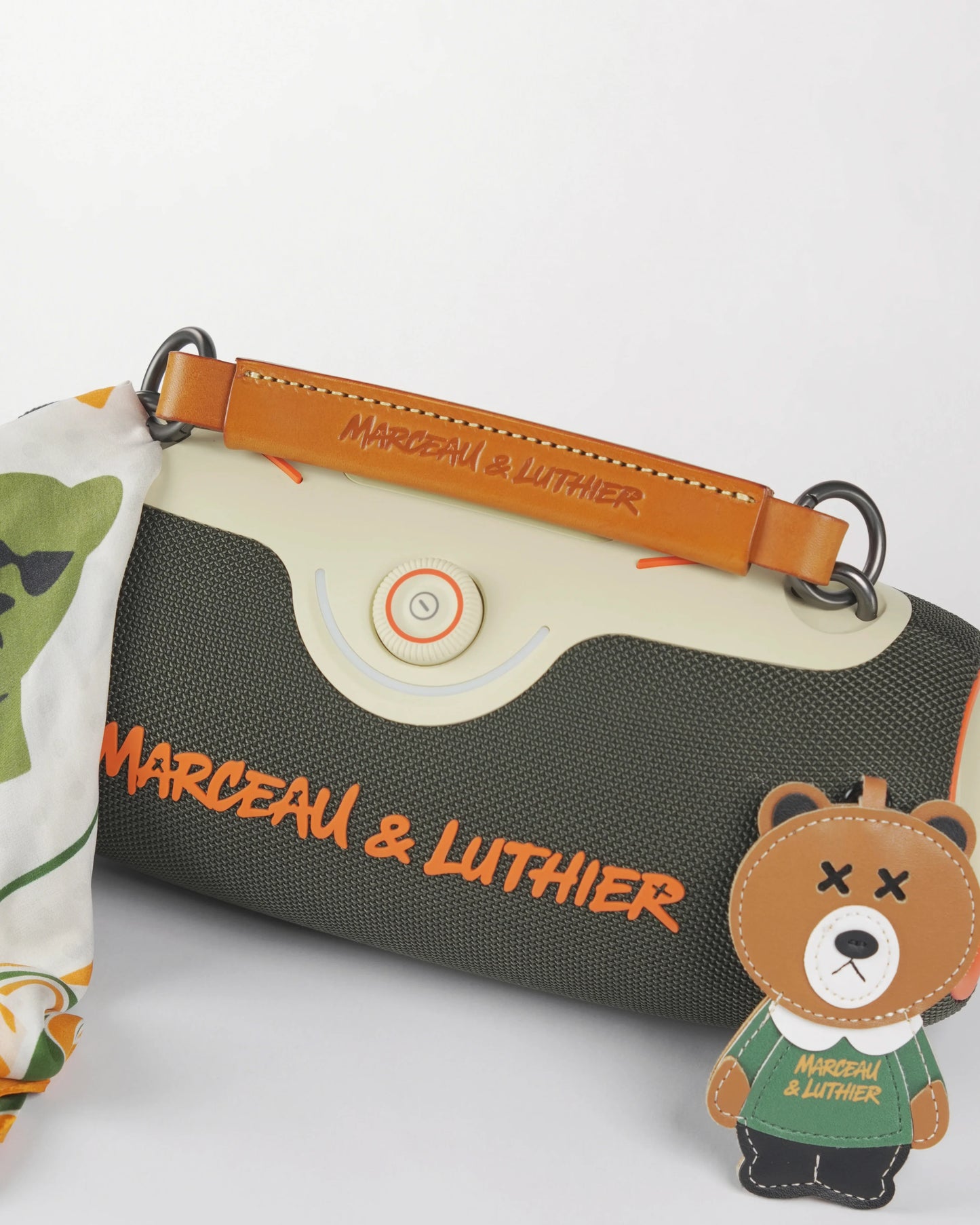 Top of the Rive Droite speaker with its leather strap, bear charm, and bandana, showcasing the rugged dark fabric.